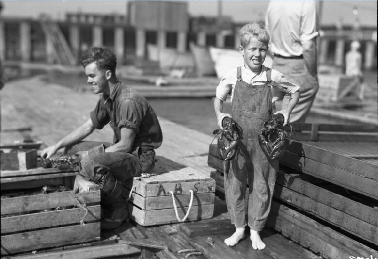 black and white photo of young boy on dock holding a live lobster in each hand