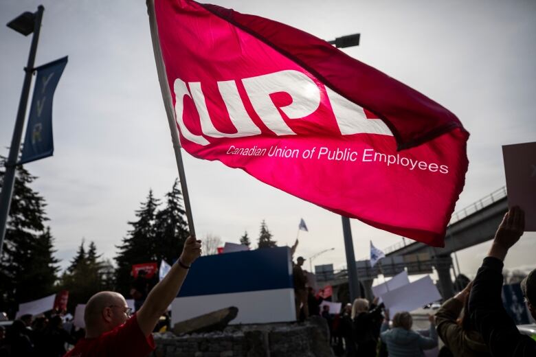 A person waves a giant red flag reading 'CUPE - Canadian Union of Public Employees.'