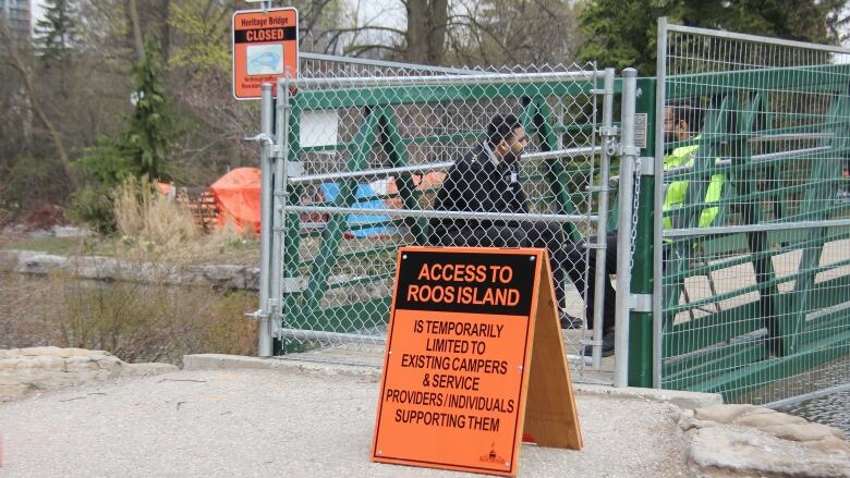 An orange sign with black writing indicates the bridge is closed. Two security officers sit behind a gate.