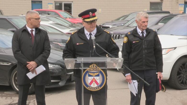 Police at a podium in front of cars.