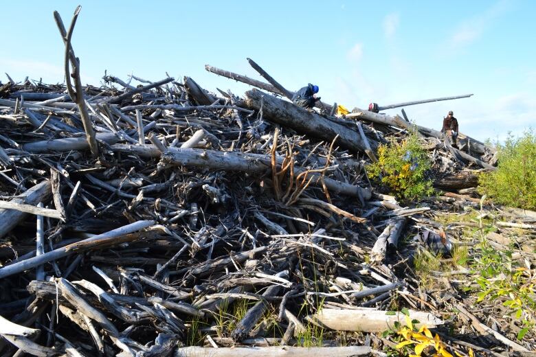 A huge pile of wood, photographer from the ground, rises up into the air. A few people can be seen standing on top of it.