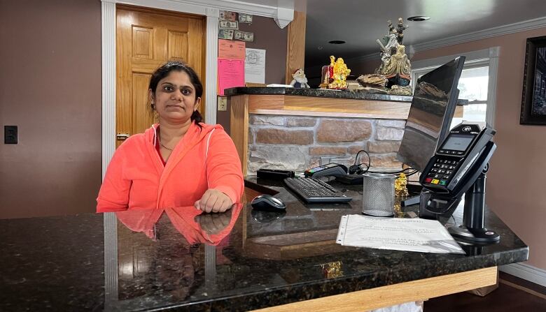 A South Asian woman stands behind a granite counter in a motel lobby.