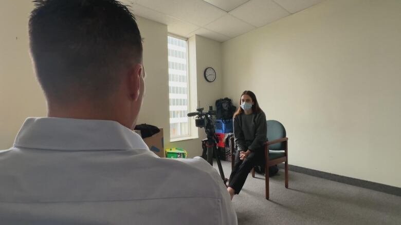 The back of a man's head is in the foreground and then a woman sits staring at the camera in the background. 