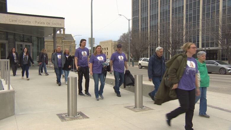 Several people, mainly in purple T-shirts walk out of a building labelled law courts.