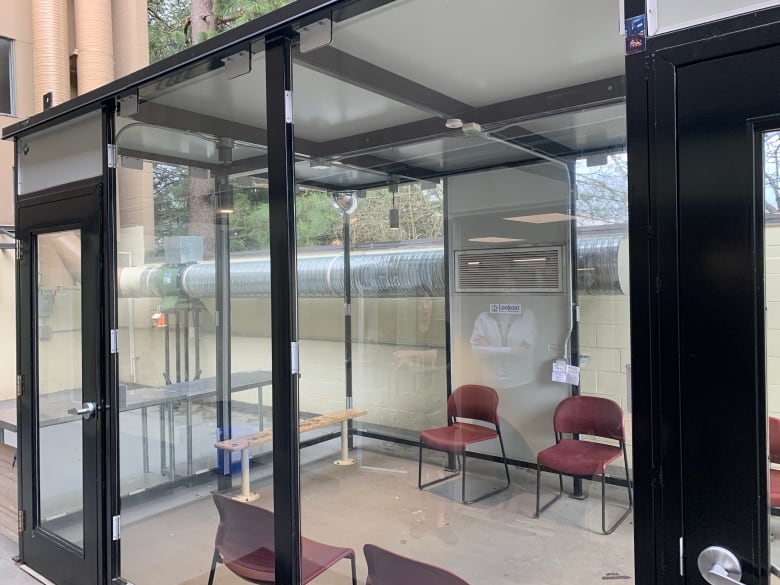 A glass-walled small building, with red plastic chairs inside. 