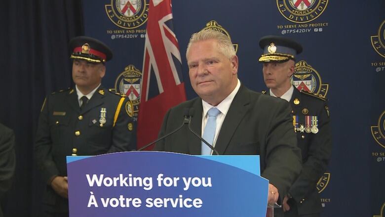 Doug Ford at a podium with two police officers in uniform behind him. 