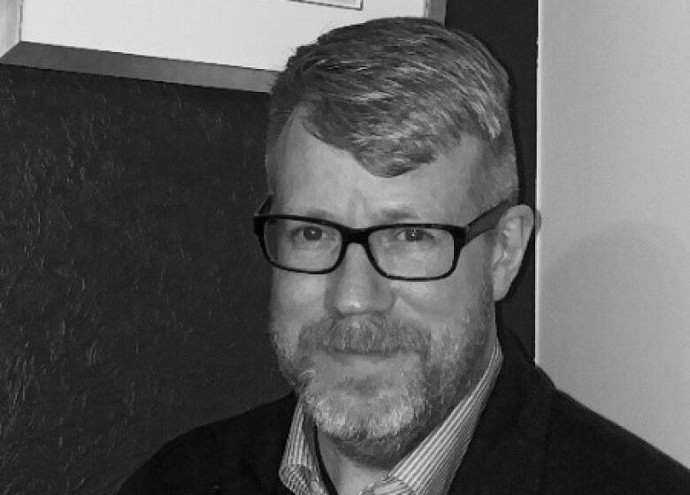 A black-and-white head-and-shoulders image of a bearded man wearing glasses.