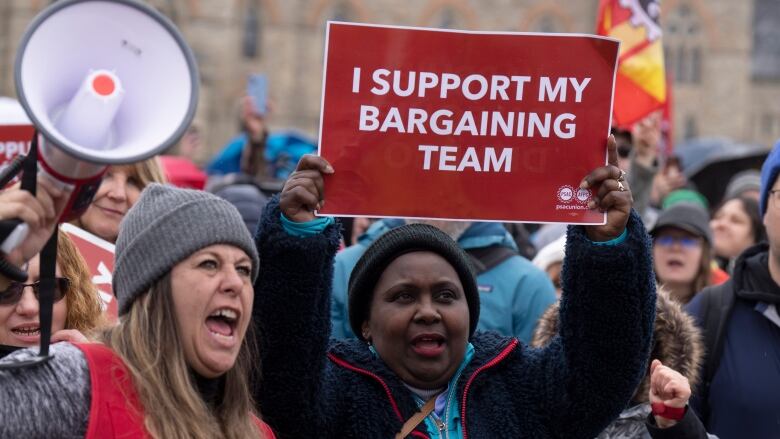 A striking public servant holds up a sign that reads 