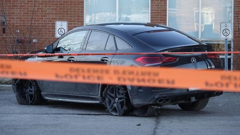 A car with punctured tires and damaged by gunshots is parked behind police tape. 