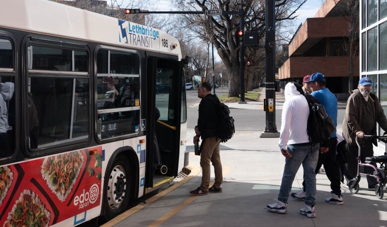 A white transit bus parked with open doors as several people walk into and towards it