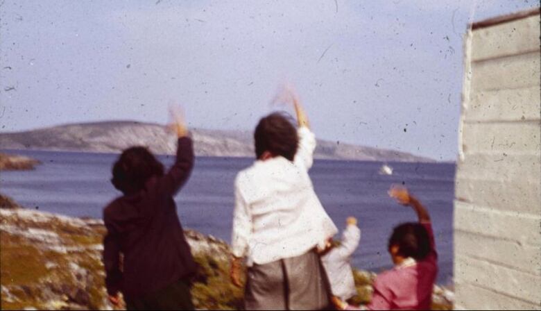 Women are shown in an archival photograph waving at boats passing by. 