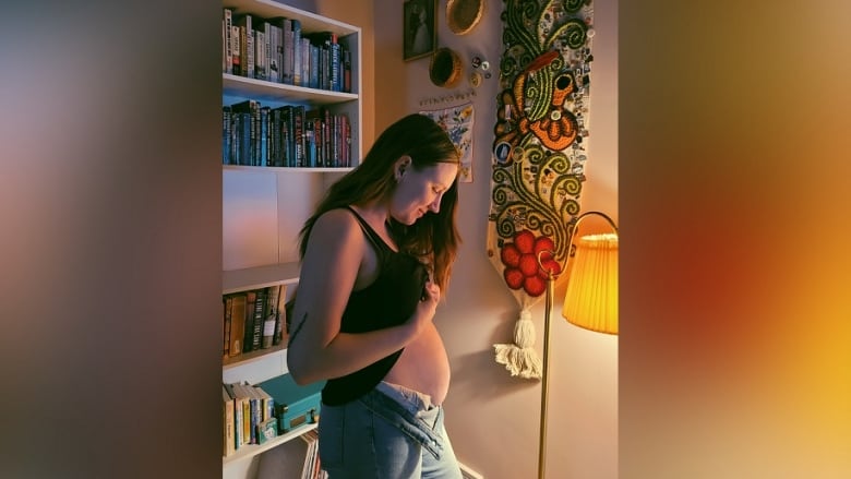 A woman lifts her shirt to show her pregnant belly.