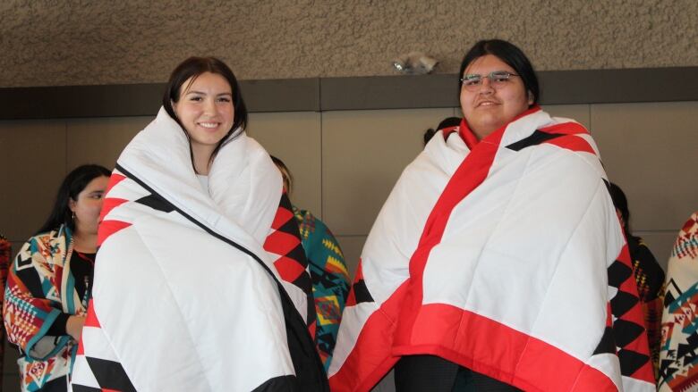 A young woman and man smile while being wrapped in a star blanket.