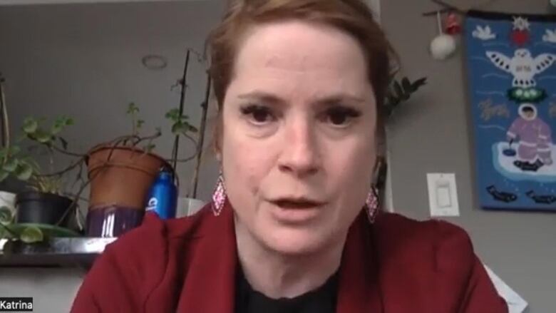 A woman in a red blazer stares straight forward, she is about to speak. 