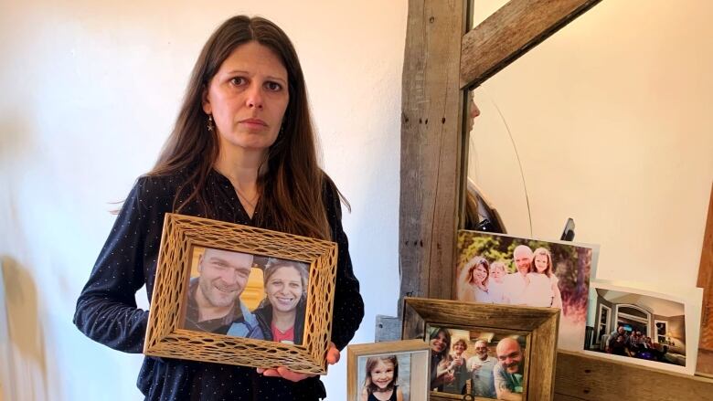 A woman stands in front of a mirror holding a photograph in a frame. 