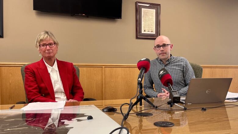 A woman and man sit behind a microphone at a conference table.