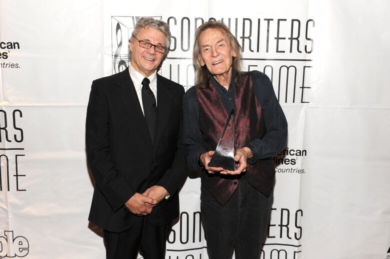 Two men are shown posing for a photograph at an event, with one holding a triangular shaped award.