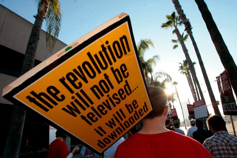 A man carries a picket sign that says the revolution will not be televised, it will be downloaded.