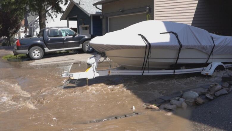 A driveway with a boat and a pickup truck is seen with pooled water.