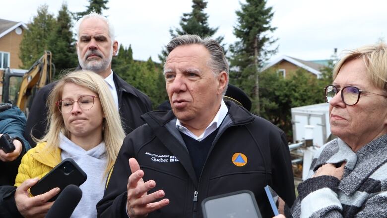 Four people stand before reporters in Baie-Saint-Paul.