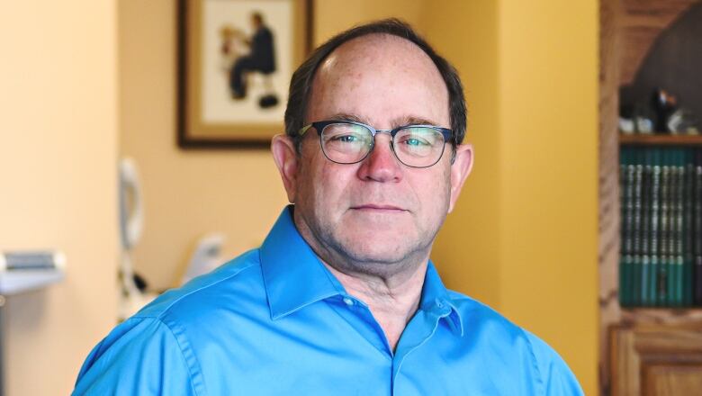 Dr. Gerry Prince wears a blue shirt and leans on a counter in his clinic. A scale can be seen in the background.