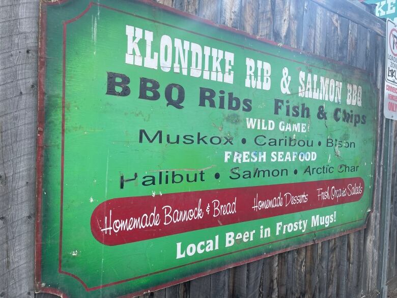 A weathered sign on the side of a building is labelled Klondike Rib and Salmon BBQ.