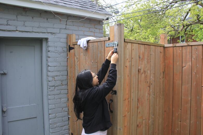 A woman reaches up to unlock a wooden fence. 