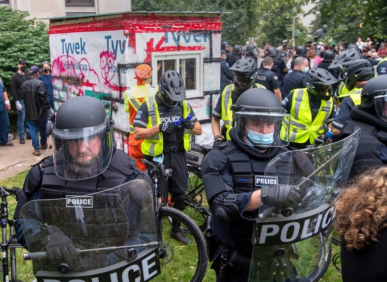 Police officers stand in front of a shelter structure during a protest.