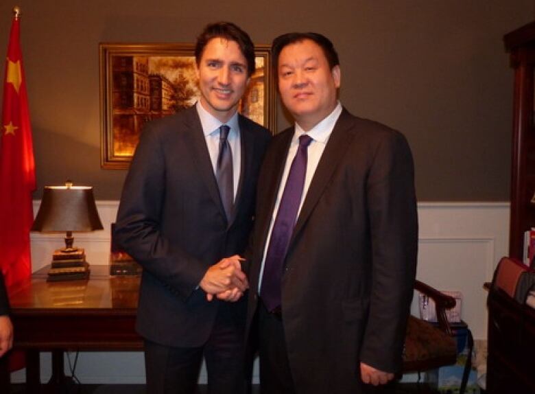 Prime Minister Justin Trudeau shaking hands with Zhang Bin, both men are wearing suits. 