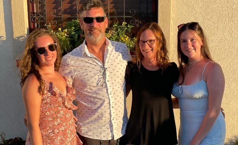 A middle-aged couple and their two adult daughters in summerwear pose for photo.