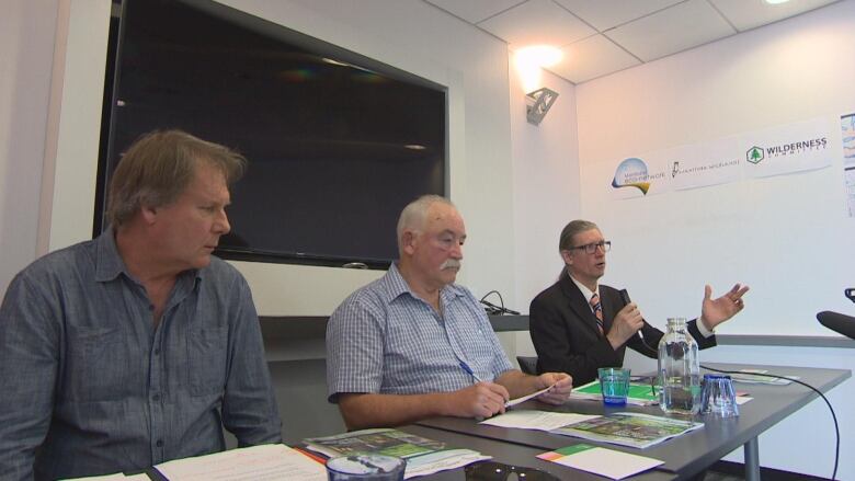 Three men sitting a table speak to media at the unveiling of a report on logging in provincial parks.