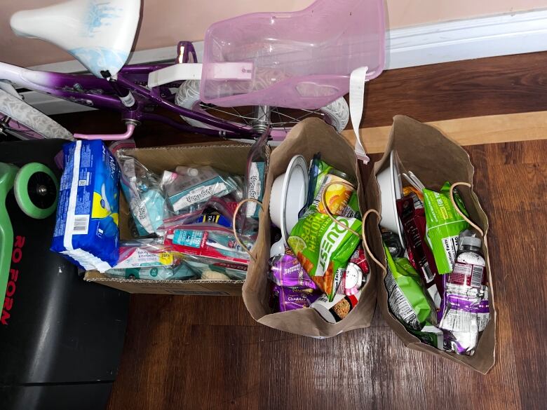 Brown paper bags filled with snacks and hygiene products sit next to a child's bicycle.