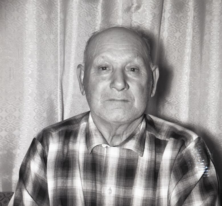 A black and white photo of an older man in a plaid shirt.