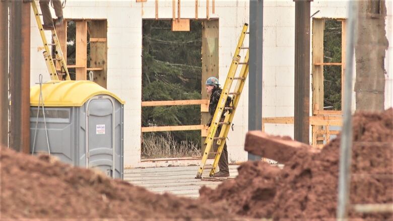 A stands at the foot of a ladder at a construction site.