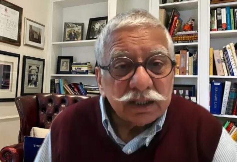 A man with a mustache and glasses speaks while sitting in an office.