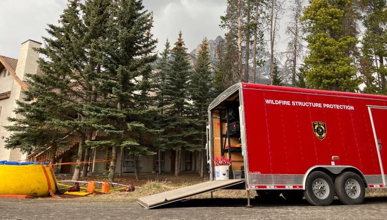 A red truck that reads 'wildfire structure protection' sits in front of trees and a mountain can be seen in the background. A circular yellow object sits on the ground nearby. 