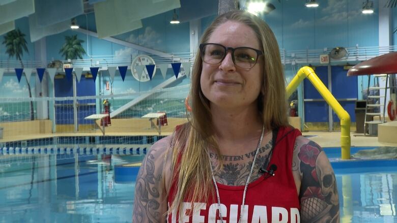 A female lifeguard stands inside an aquatic centre.