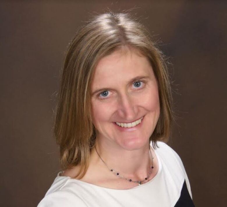 A woman wearing a white shirt with brown hair smiles at the camera.