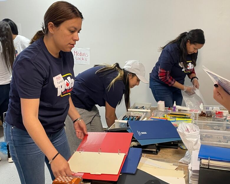 Woman holds a binder while looking at a table covered in folders, binders, pencils and other school supplies