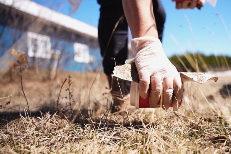 A hand is shown picking up a Tim Hortons cup from the ground. 