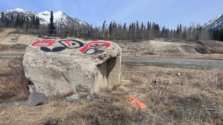 Am empty lot with a large piece of concrete decorated with Indigenous paintings. There are mountains in the background.