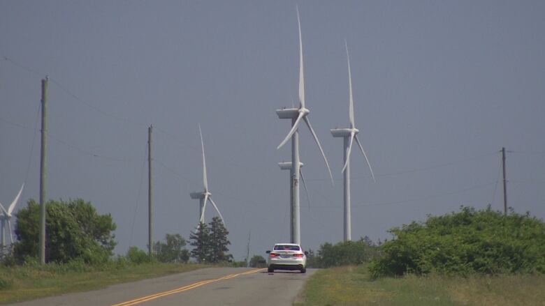 Wid turbines near a road, with a car driving by for scale.