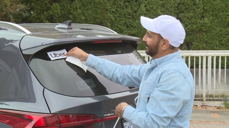 Ride-hail driver placing Uber sticker on vehicle.