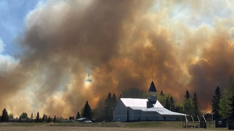 A church with a large plume of orange smoke behind it. 