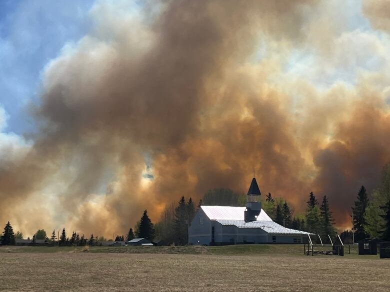 A church with a large plume of orange smoke behind it. 