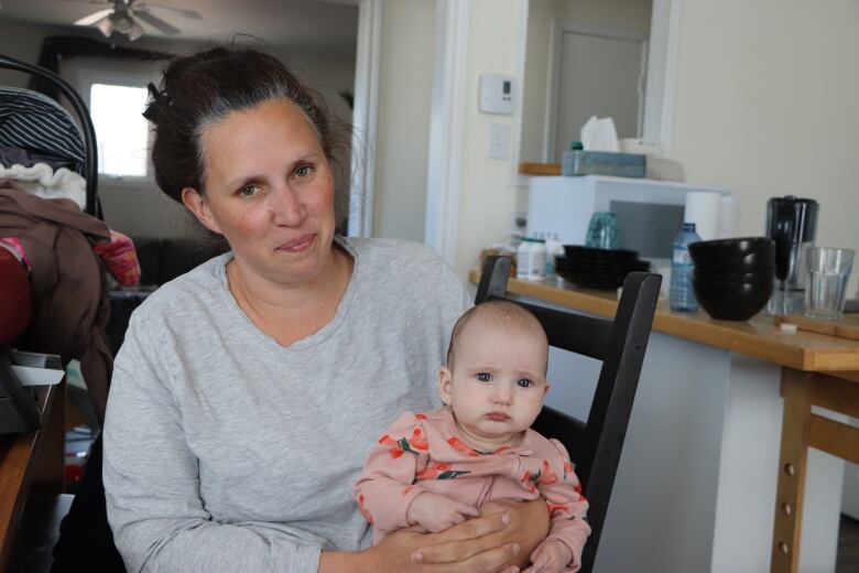 A mother sits on a chair holding her baby who is facing the camera. 