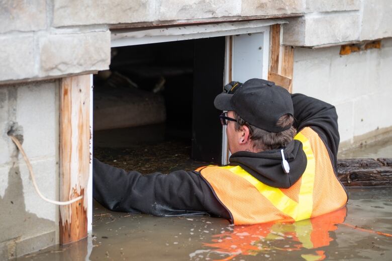 Someone looks through an opening to a basement apartment in chest-deep water.