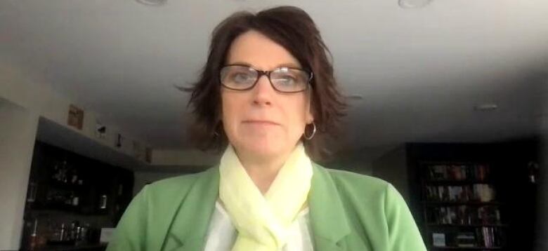 A woman with dark hair and glasses sits in front of a computer screen.