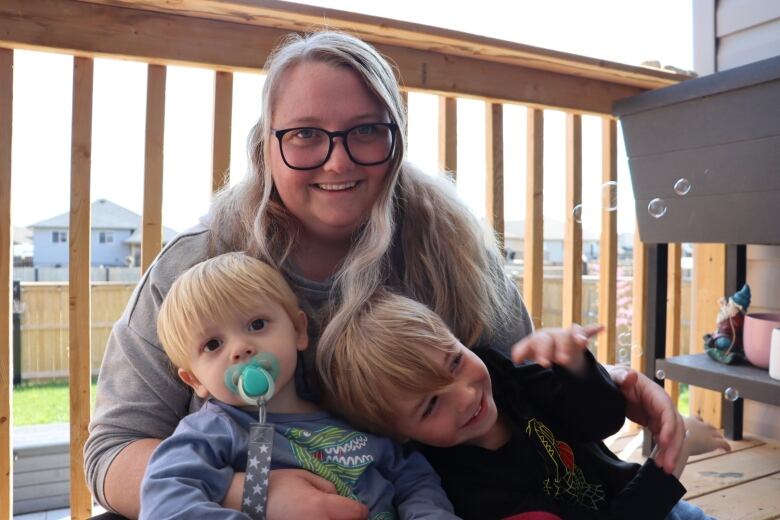 A woman sits with her two children on a porch.