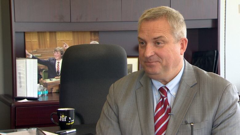 A man wearing a grey suit looks to the left of the camera.